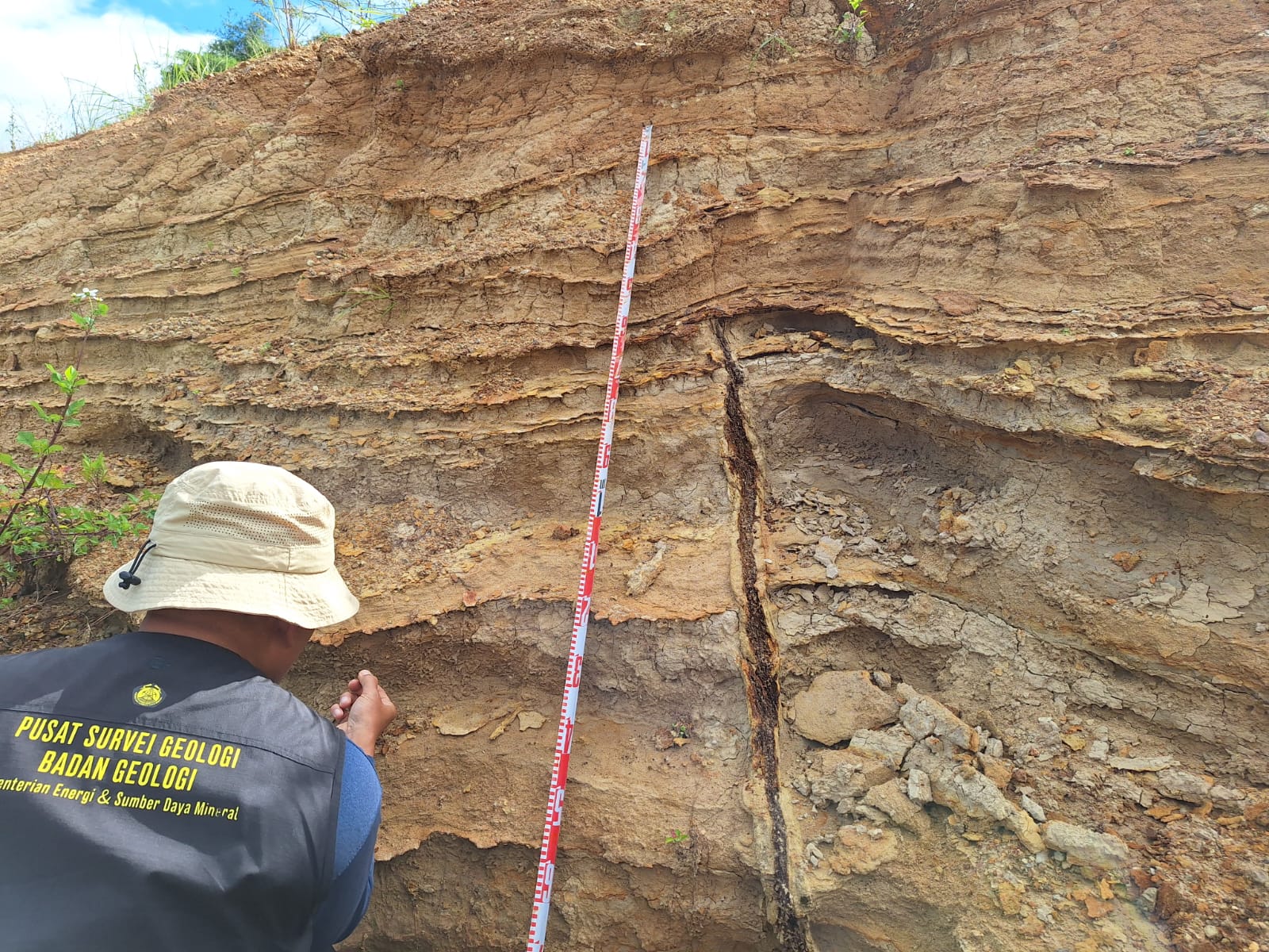 Pengukuran dimensi singkapan pada lapisan perulangan tuf menghalus ke atas (graded-bedding) dengan lapisan oksida besi di bagian bawahnya, terlihat terpotong oleh sebuah kekar (retakan)